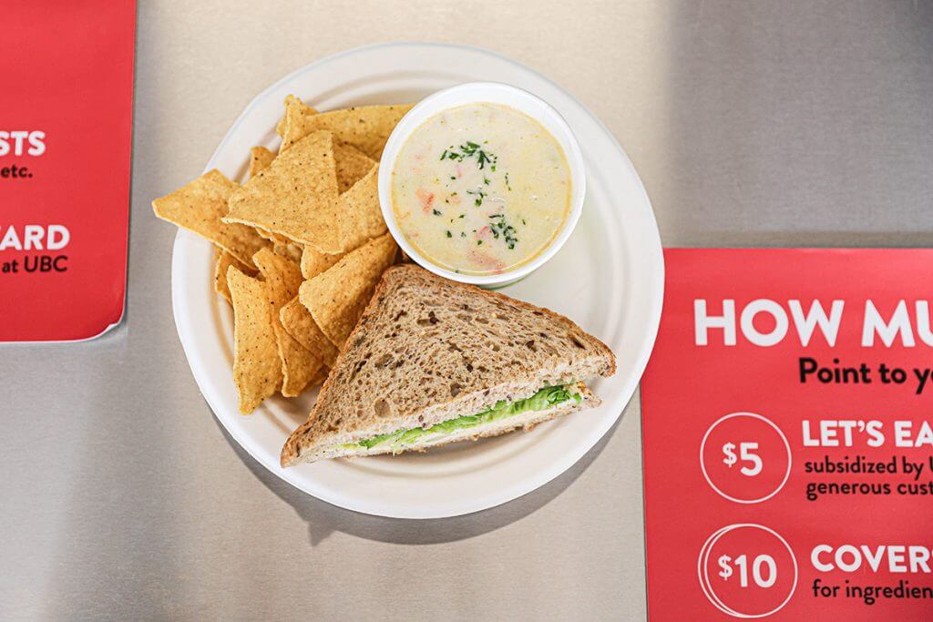 Sandwich, soup, and corn chips served on a paper plate